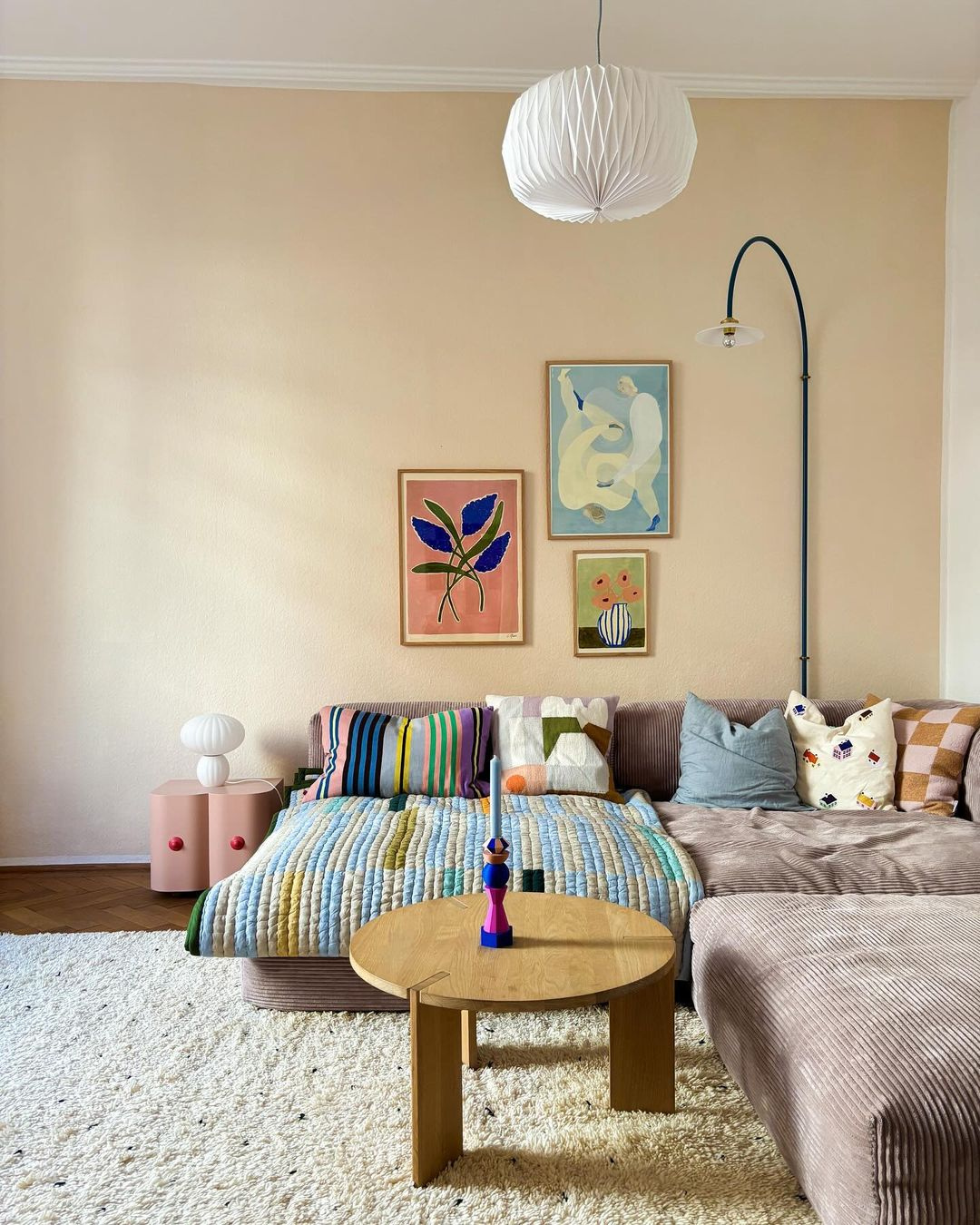 Living room with ANIS candleholer on the table, a beige wall, colorful artwork, and a sofa with patterned cushions.
